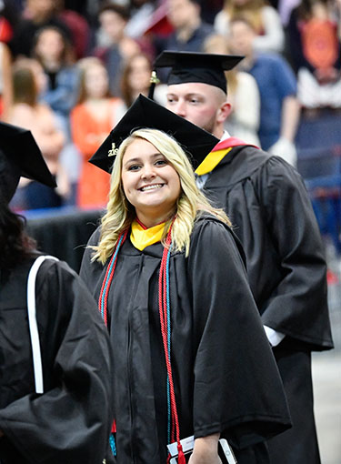 A Fisher student smiles in cap and gown entering the Blue Cross Arena during Commencement.