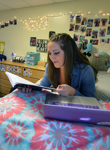 A Fisher student studies on her bed in a dorm room.