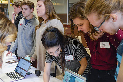 Students gather around laptops to view the work of their peers during the annual scholarship symposium.